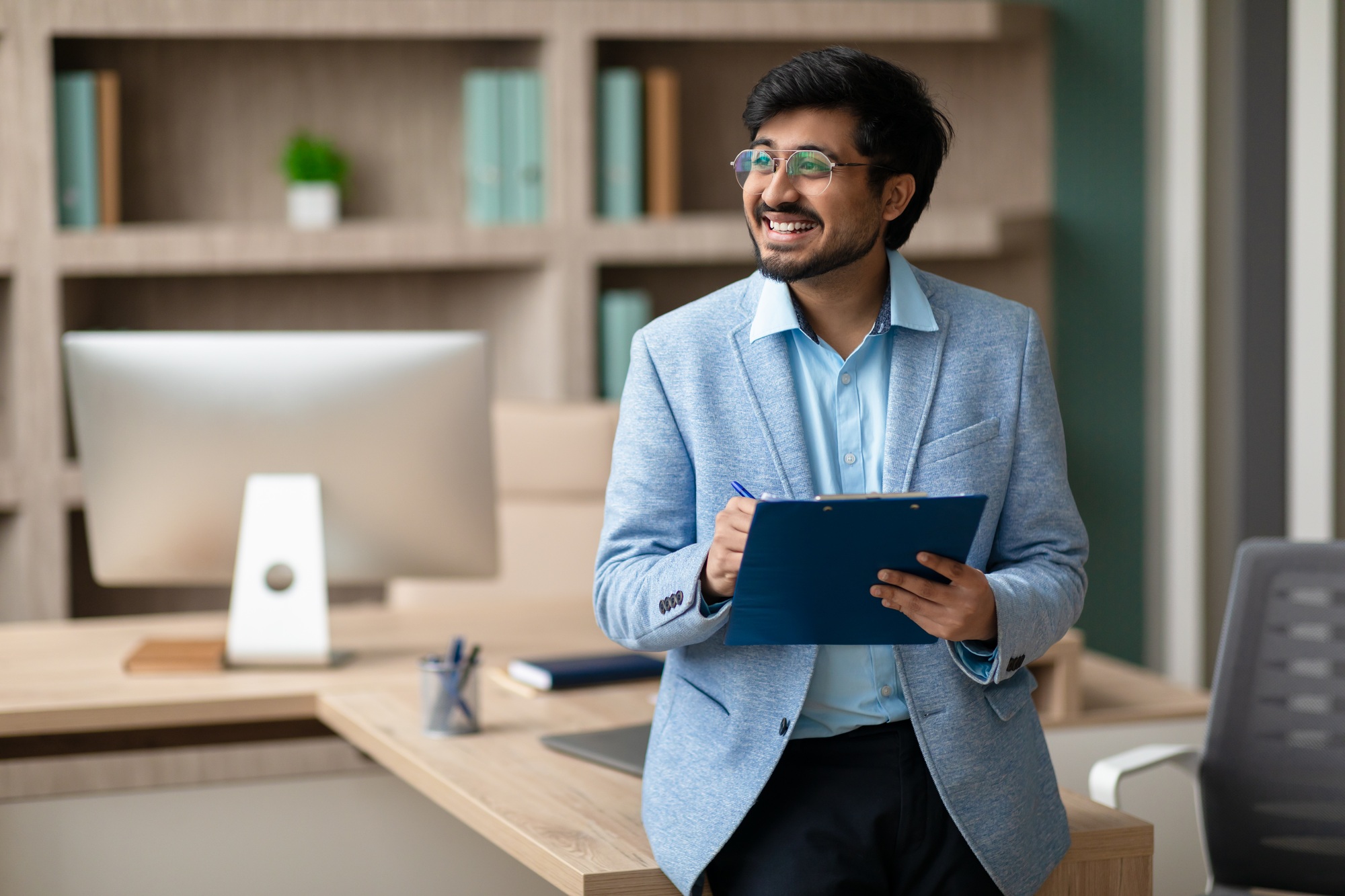 cheerful-indian-professional-businessman-holds-clipboard-and-signing-documents-indoor